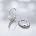 Classic Silver Drop Hoop Earrings, two polished silver hoop earrings lying on a pale grey surface