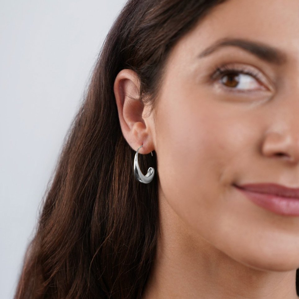 Classic Silver Drop Hoop Earrings, worn on an ear of a woman with long dark hair, polished silver
