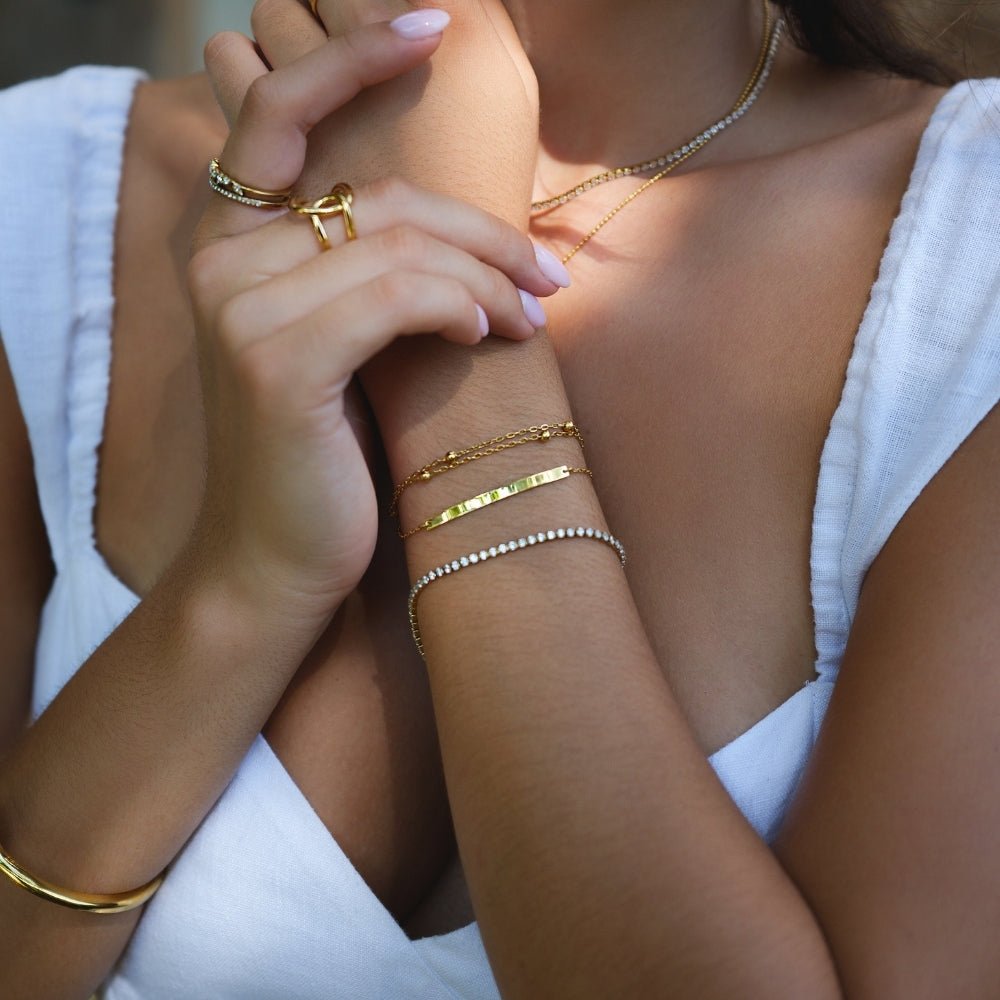 Cordelia Gold Tennis Bracelet, worn on a wrist with stacked gold bracelets and rings