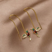 Crystal Hummingbird Tassel Earrings, a pair of gold hummingbird earrings on a tan satin cloth