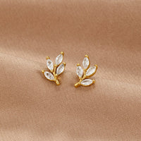 Crystal Leaf Stud Earrings, a pair of gold leaf studs with clear marquise stones on beige fabric