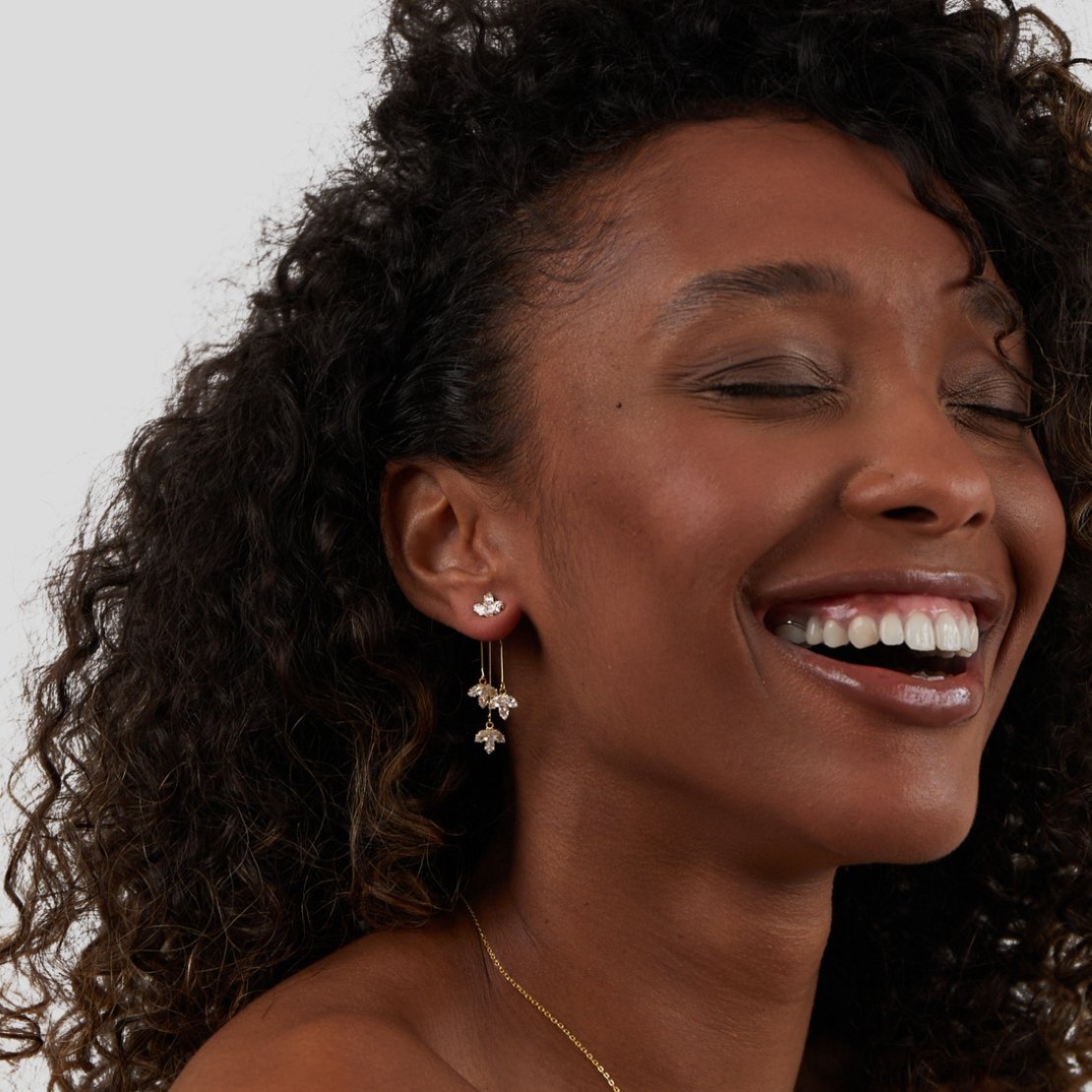 Crystal Lotus Waterfall Earrings, worn by a smiling model with curly hair, eyes closed