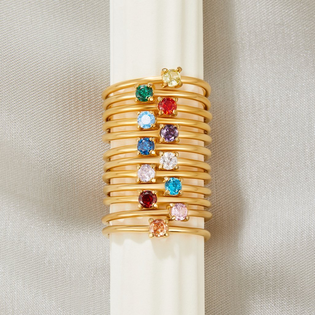 December Birthstone 18K Gold Ring, stacked on a white cylinder with many gold bands and