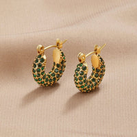 Emerald Beauty Hoop Earrings, a pair of gold hoop earrings set with green stones, resting on a