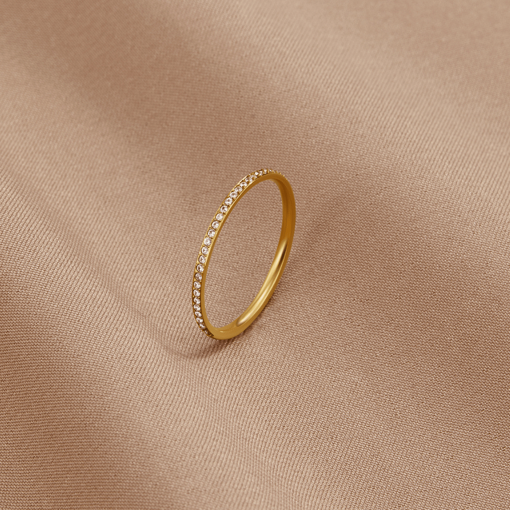 Eternity 18K Crystal Ring, standing upright on beige fabric, gold band with a row of small crystals