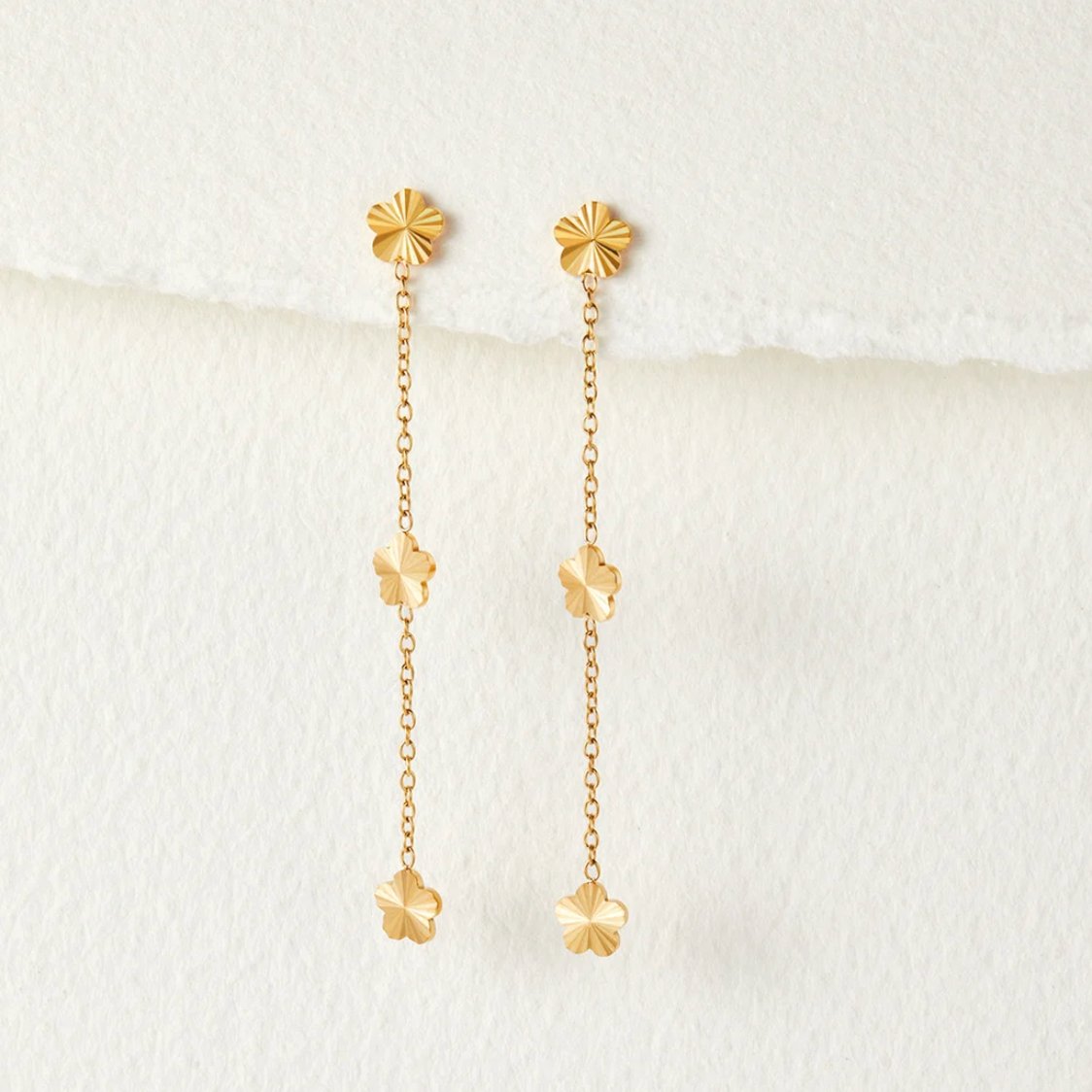 Flower Power Petal Drop Earrings, pair of gold flower drop earrings hanging on white textured