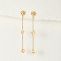 Flower Power Petal Drop Earrings, pair of gold flower drop earrings hanging on white textured