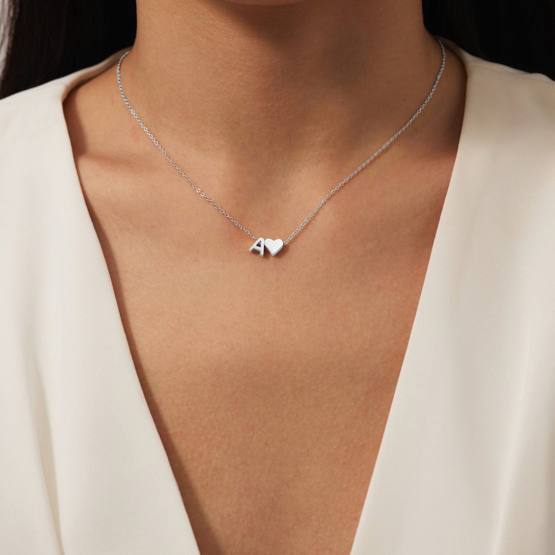 Forever Love & Letter Silver Necklace, worn on a neck with a white V-neck top, letter A and heart charm