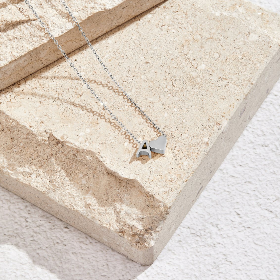Forever Love & Letter Silver Necklace, silver chain necklace laid on a stone slab, with letter