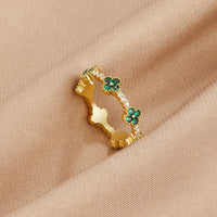 Four Leaf Clover Crystal Ring, gold band with green clover motifs on beige fabric