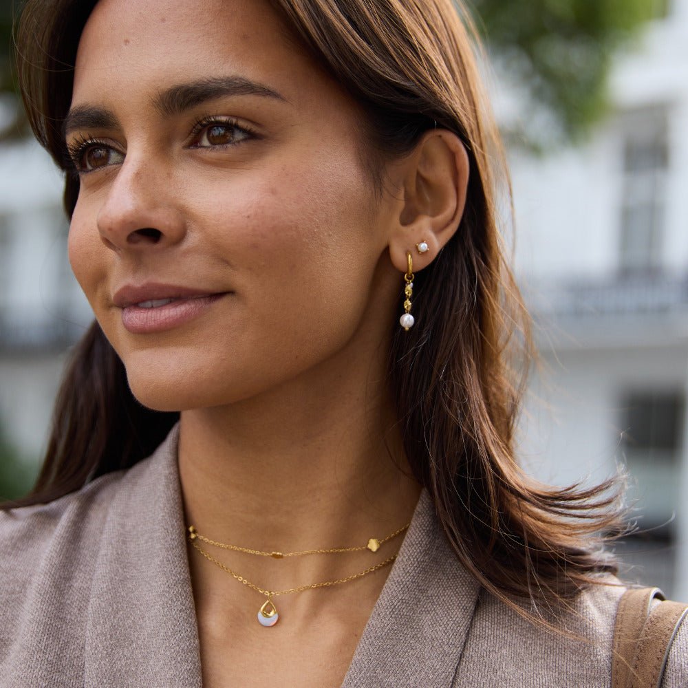 Free Sofia Pearl Stud Earrings, worn on a woman with gold drop earrings and layered necklaces