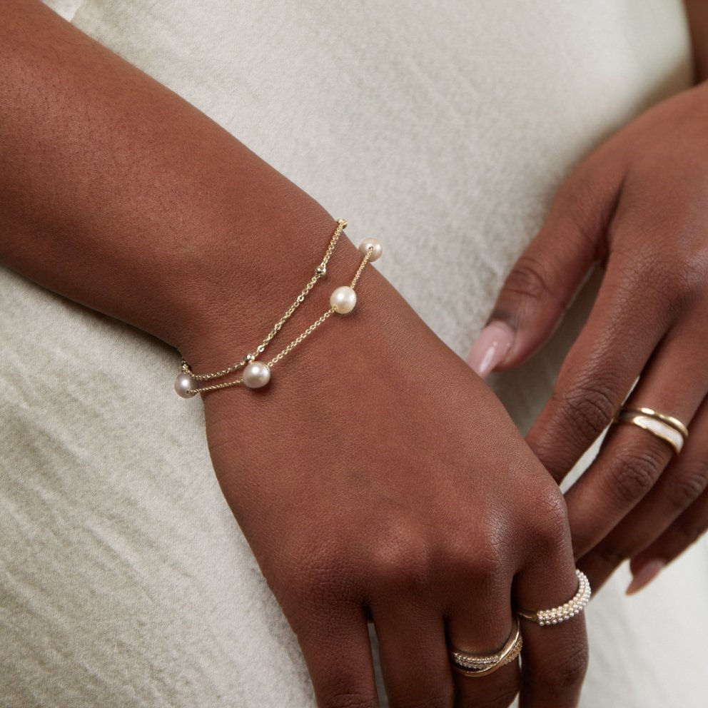 Freshwater Pearl Layered Bracelet, worn on a wrist with pearls and rings, cream top behind