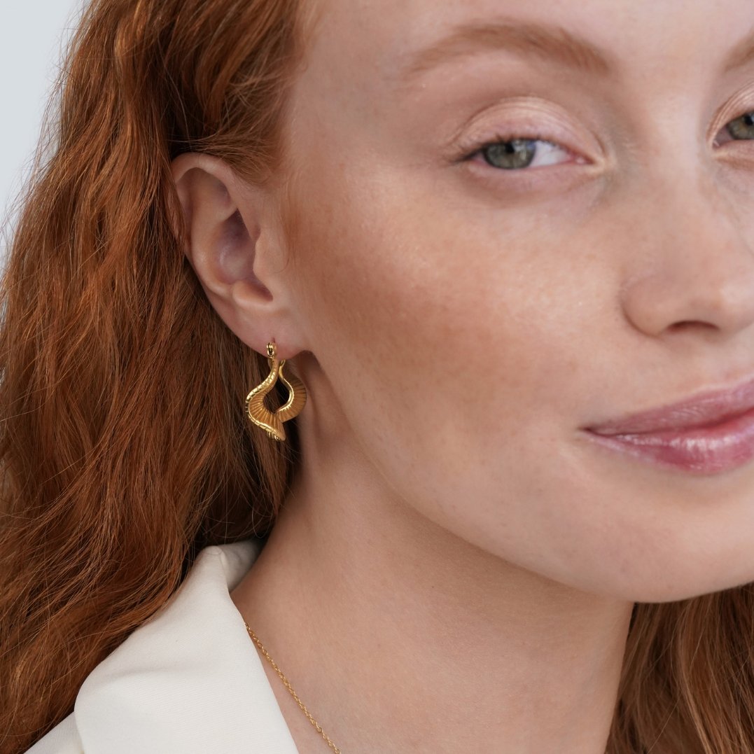 Geometric Wave Gold Hoop Earrings, worn on an ear of a model with red hair, gold ridged twist