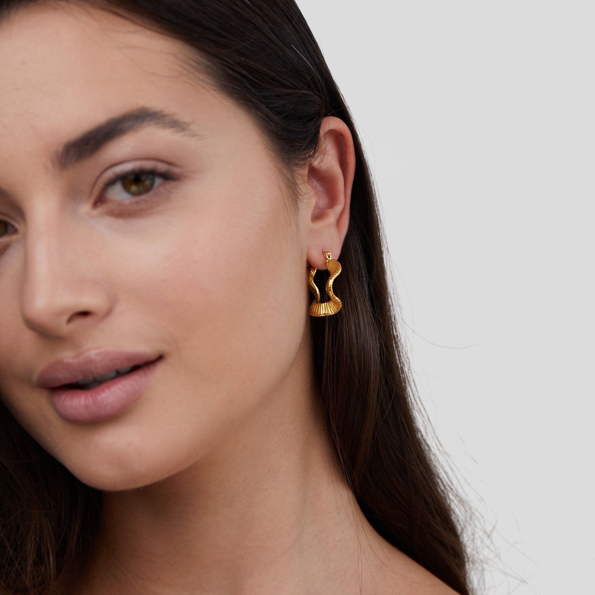 Geometric Wave Gold Hoop Earrings, worn on a woman's ear, gold snake-shaped hoop with ridged detail