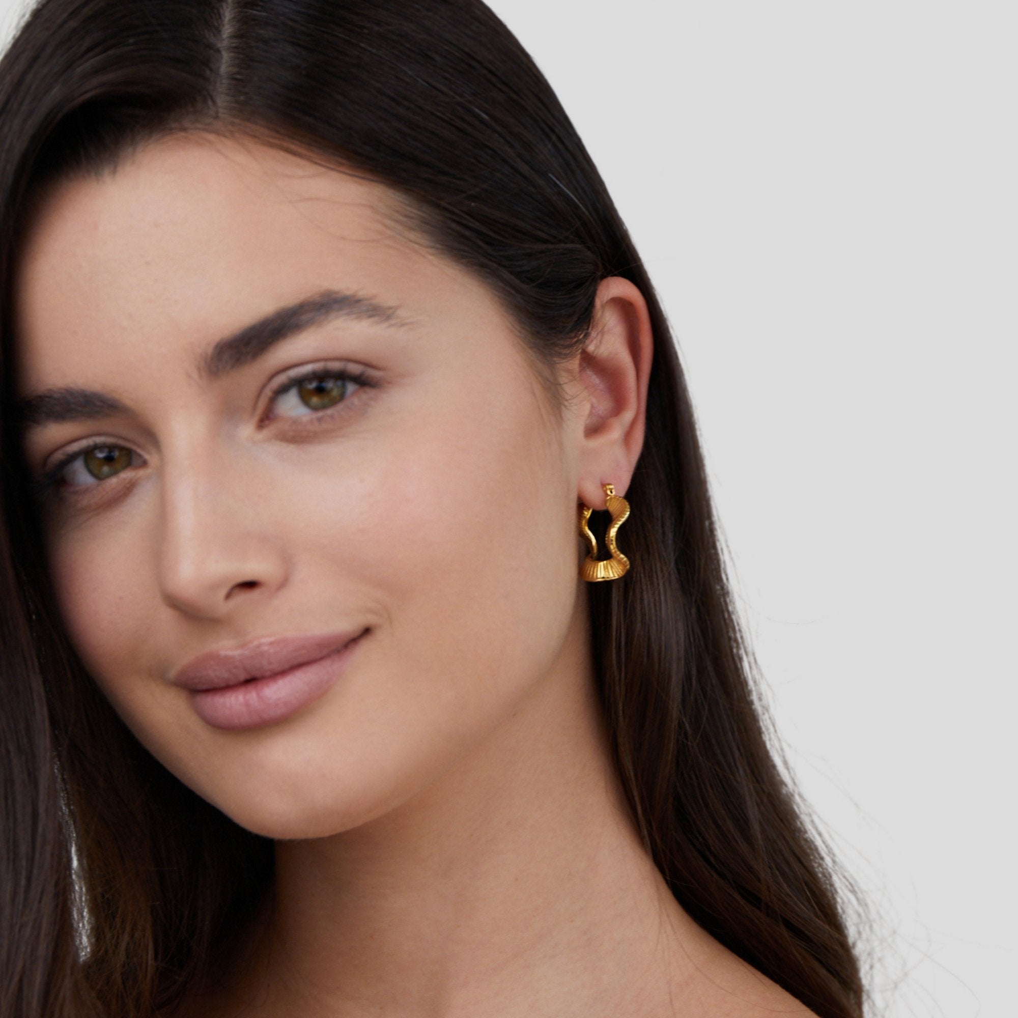 Geometric Wave Gold Hoop Earrings, worn on a model's ear, gold wavy hoop with ridged detail