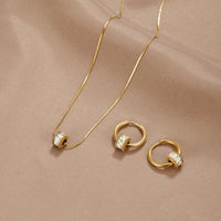 Gigi 18K Gold Set, flat-laid on a beige satin cloth, necklace and two hoop earrings