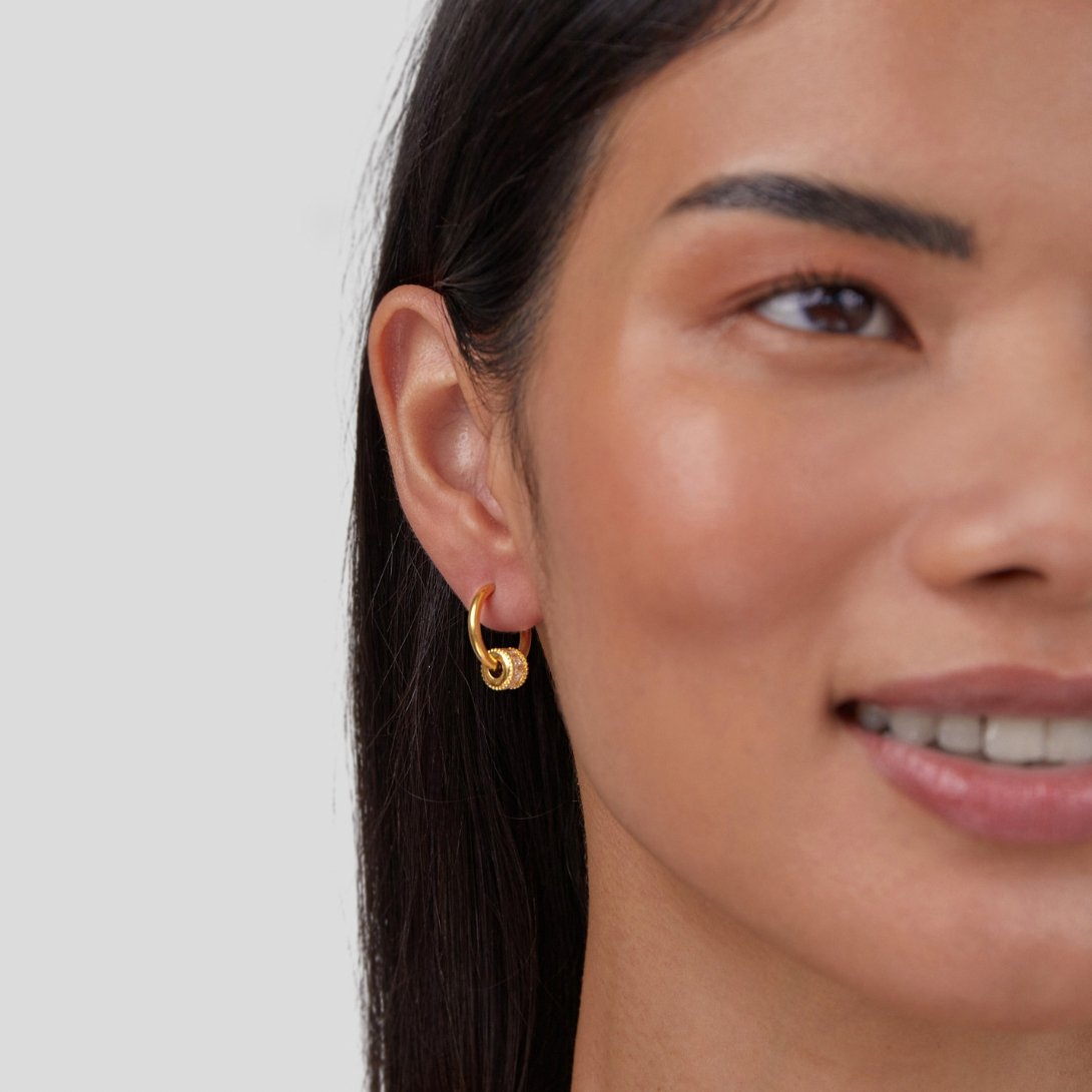 Gigi Crystal 18K Gold Hoop Earrings, worn on an ear by a smiling woman with long dark hair