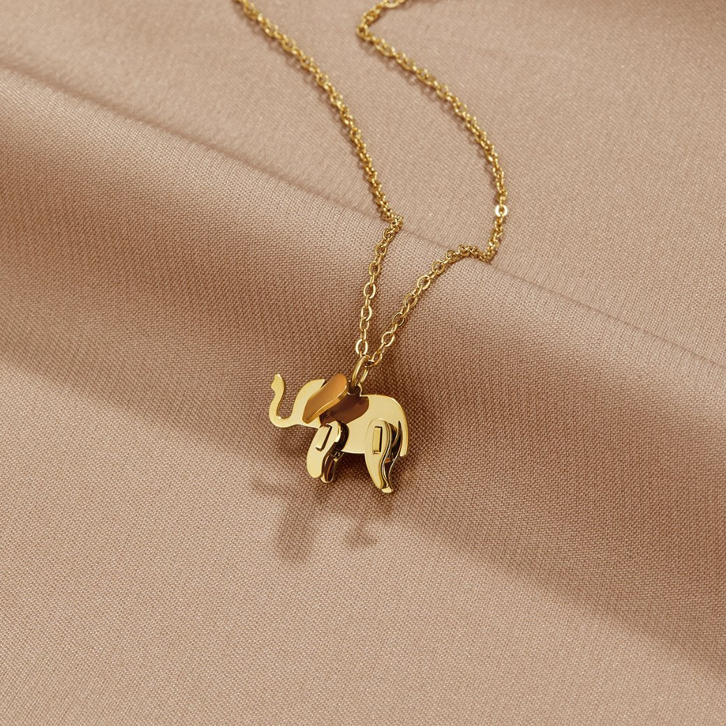 Gold Elephant Necklace, laid flat on a draped beige satin cloth, gold elephant pendant