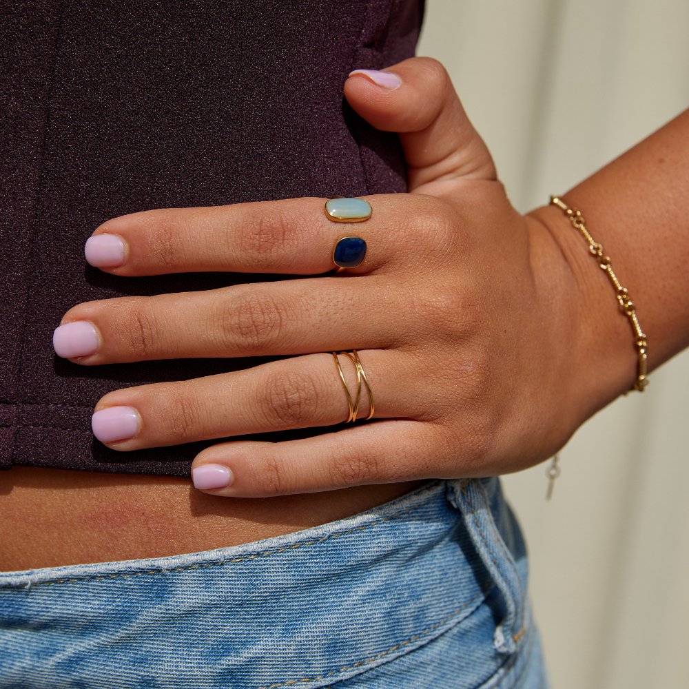 Gold Infinity Loop Ring, worn on a hand with a gold bracelet and a blue-and-pale-stone ring