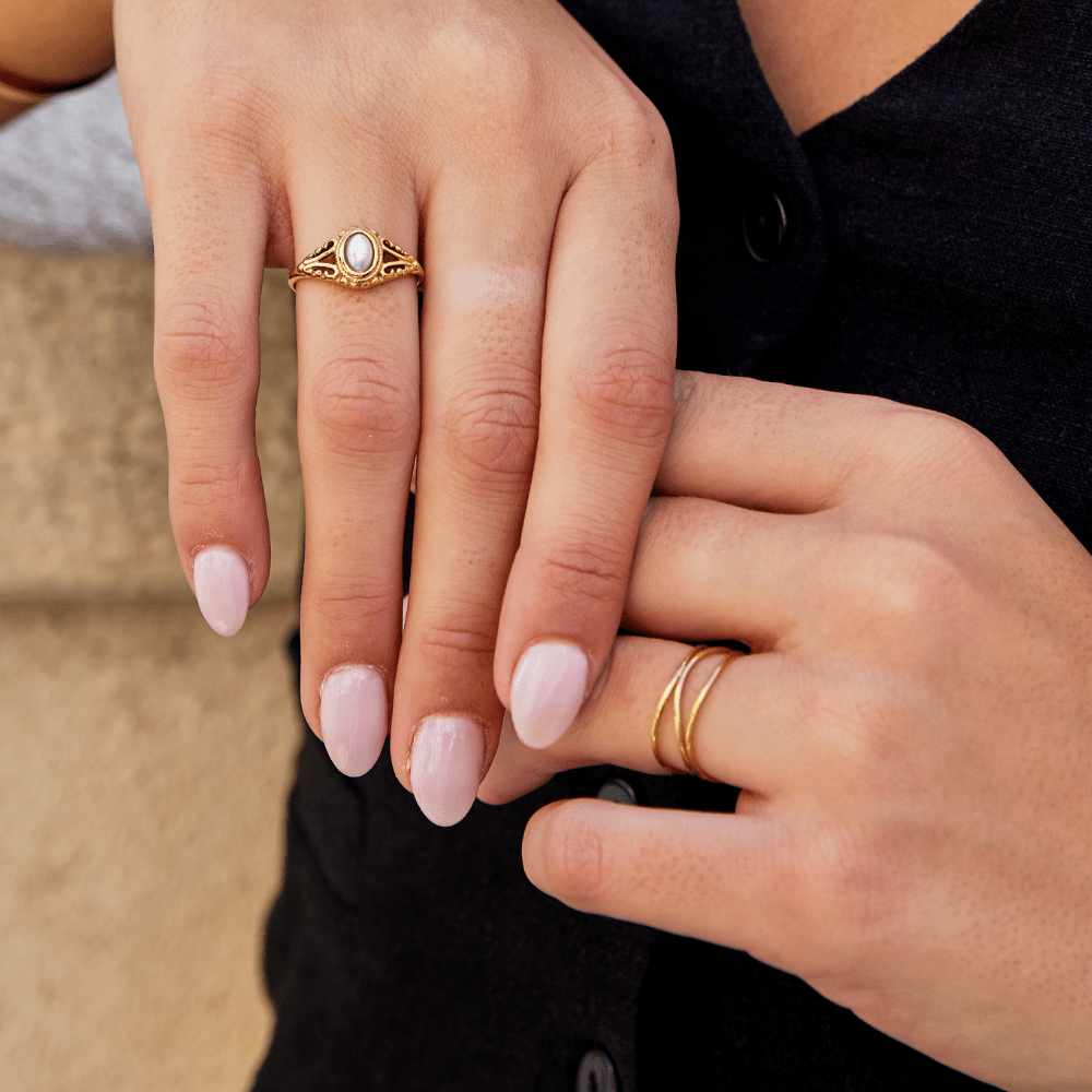 Gold Infinity Loop Ring, worn on a hand with pale pink nails, beside a vintage-style ring