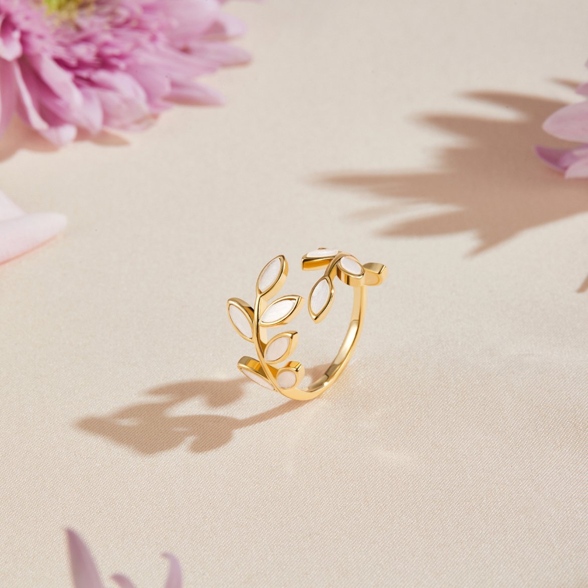 Gold Leaf Ring, standing alone on cream fabric beside pink flowers and shadows