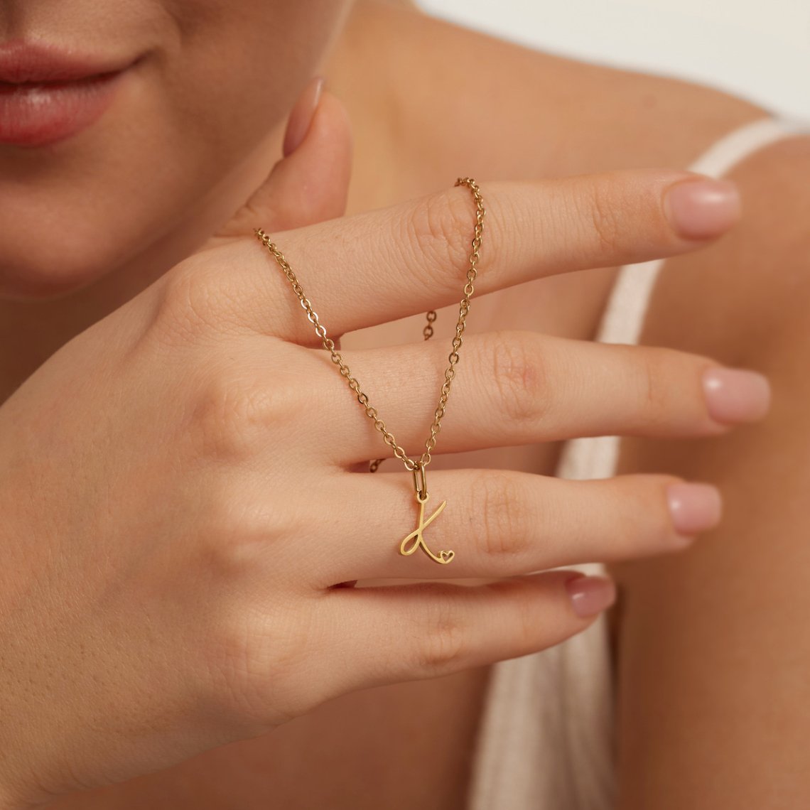 Gold Letter Heart Necklace, worn on a hand near the chin, gold script letter K pendant