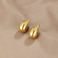 Amara Gold Teardrop Earrings, pair of polished gold teardrop earrings lying on beige satin