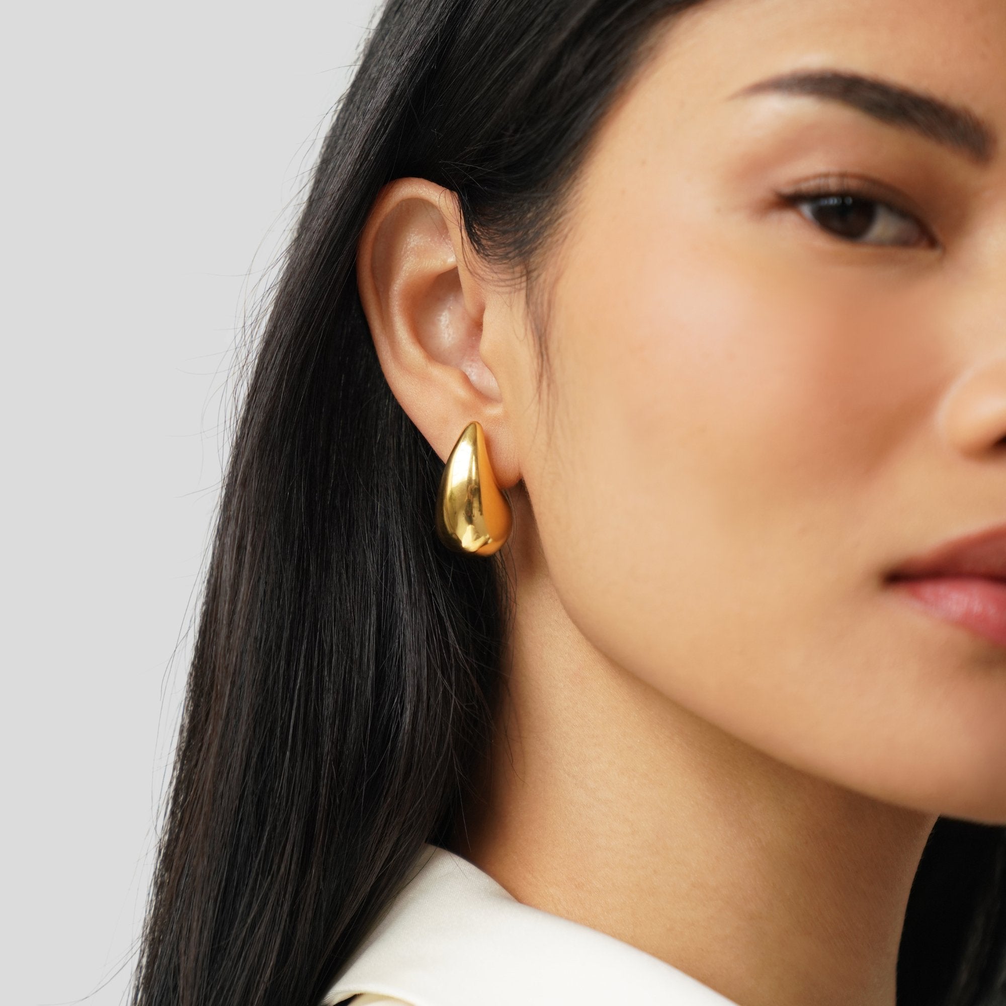 Amara Gold Teardrop Earrings, worn on an ear by a model with long dark hair, polished gold