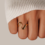 Gold Wave Ring, worn on a finger in a cream knit sleeve, gold wavy band