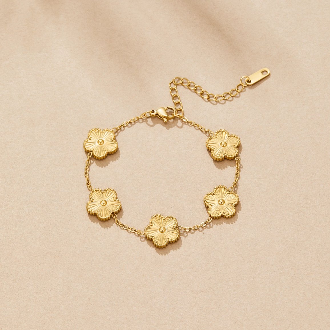 Golden Clover Bracelet, flat lay on beige fabric, five gold flower charms on a chain