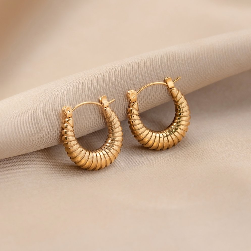 Golden Mia Croissant Hoop Earrings, a pair of gold ribbed hoops lying on a beige satin fabric