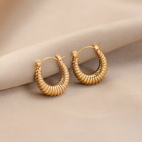 Golden Mia Croissant Hoop Earrings, a pair of gold ribbed hoops lying on a beige satin fabric