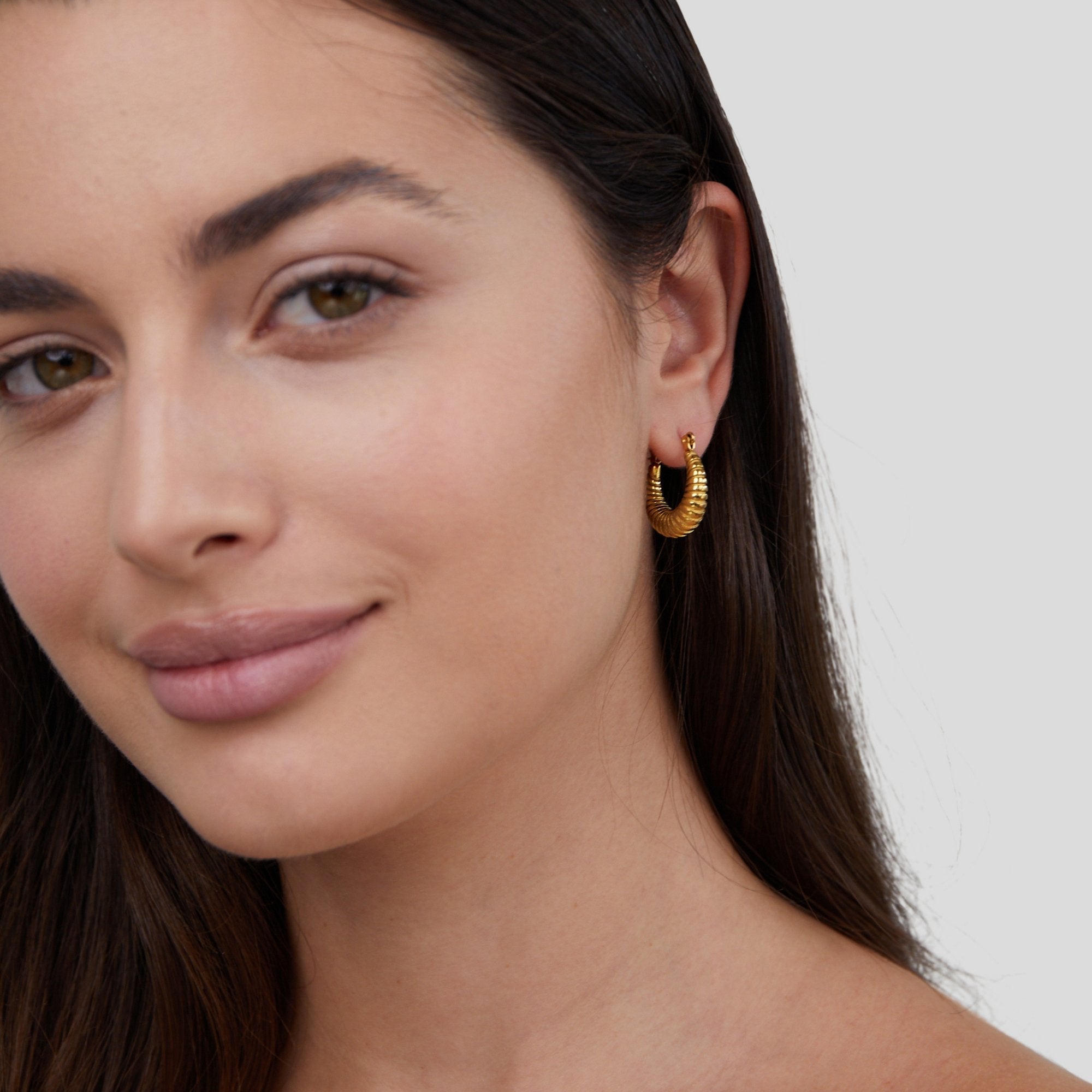Golden Mia Croissant Hoop Earrings, worn in one ear on a model with dark hair, close-up