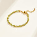 Green Peridot Bead Bracelet, laid flat on cream surface, green faceted beads with gold spacers