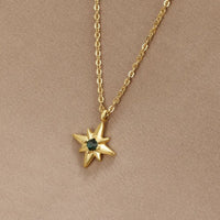 Guiding Star Emerald Crystal Necklace, worn on a beige fabric backdrop, gold chain with star