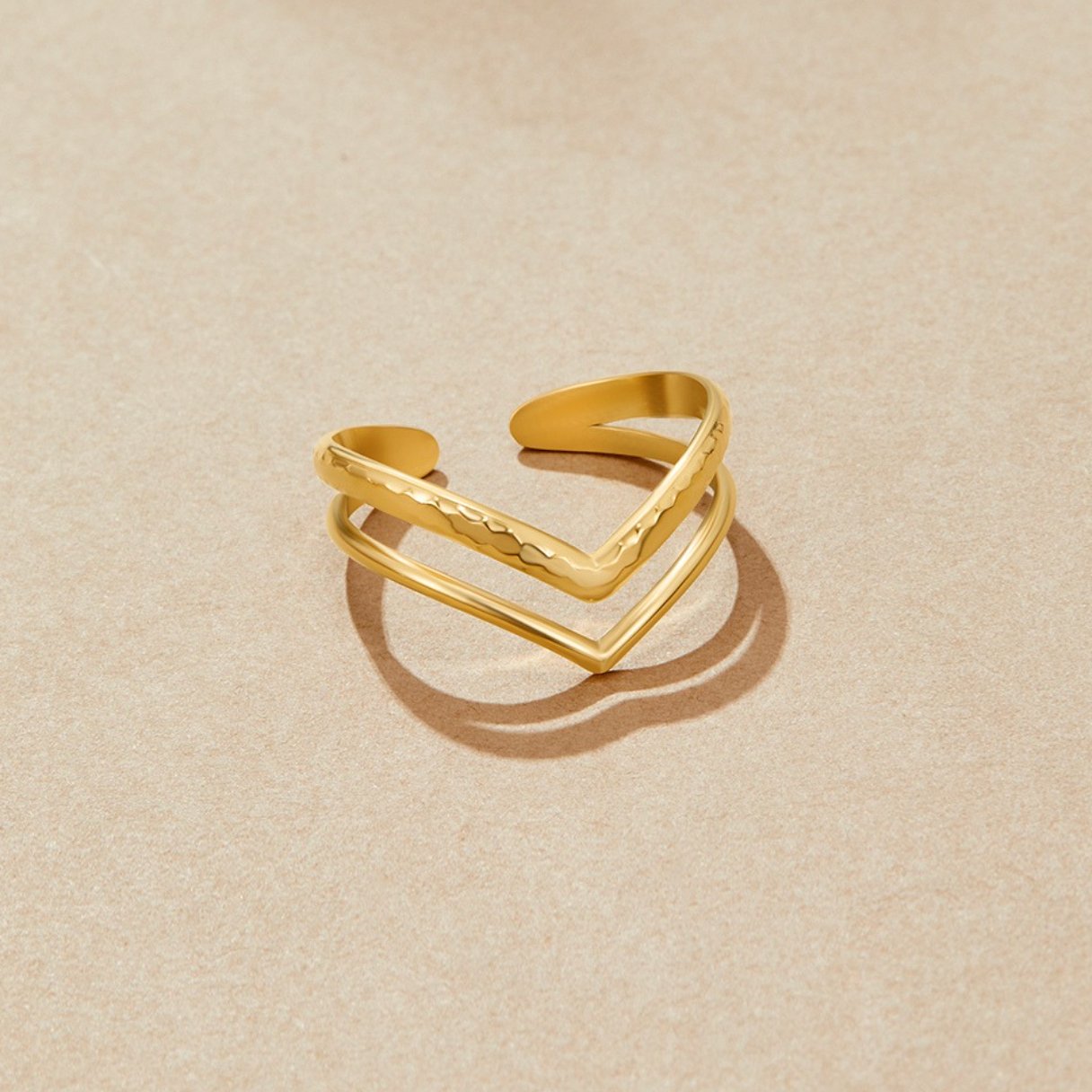 Harper Layered Wrap Ring, two gold chevron bands on a beige surface, one hammered and one smooth