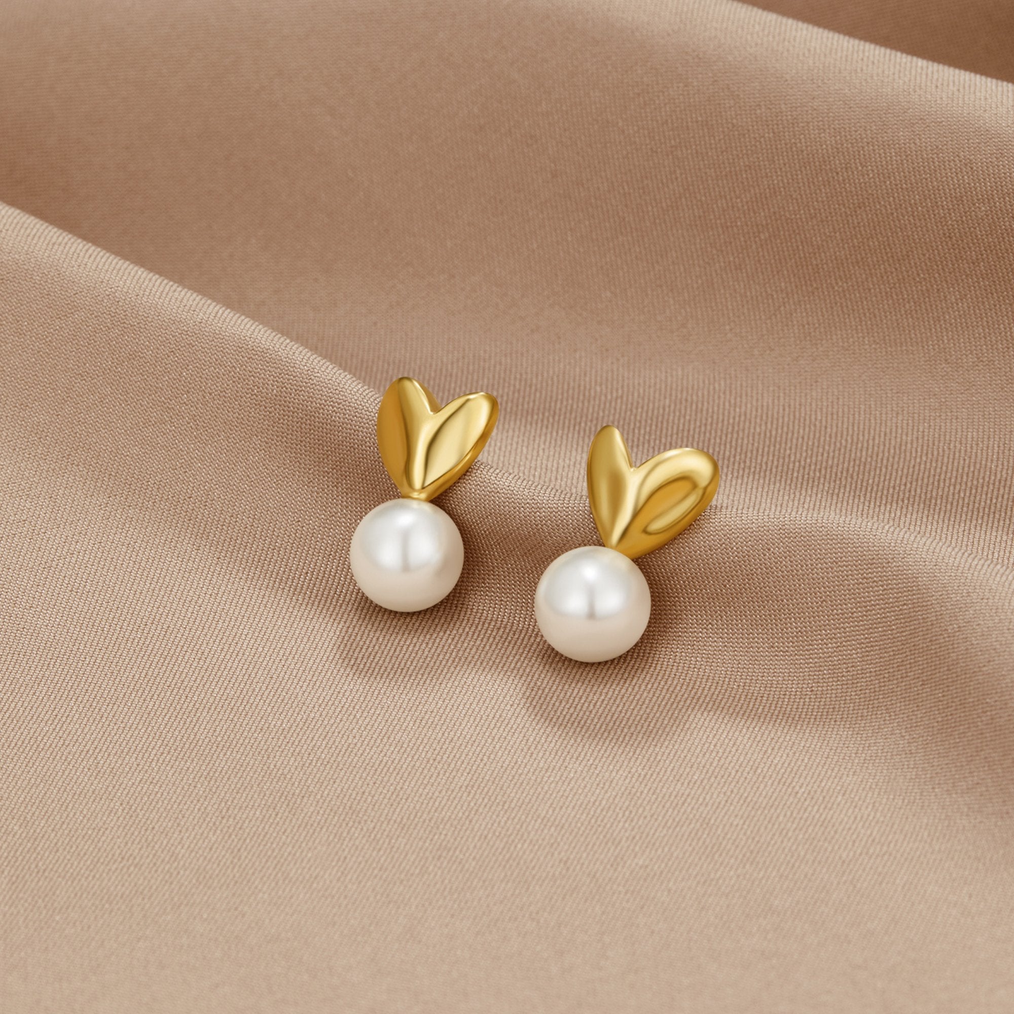 Heart & Pearl Earrings, a pair of gold heart-shaped earrings with white pearls on beige satin