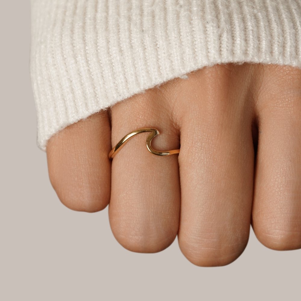 Imari Gold Wave Ring, worn on a hand in a cream knit sleeve, gold wave design