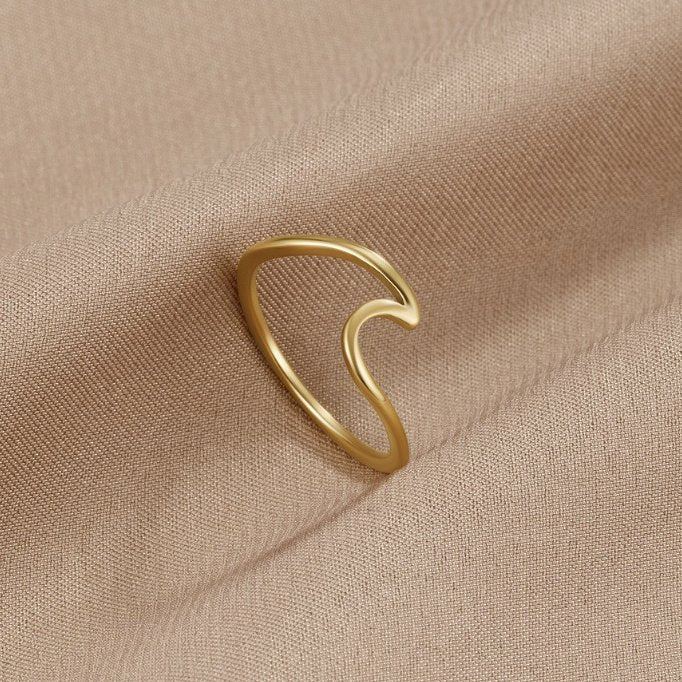 Imari Gold Wave Ring, lying on draped beige fabric, polished gold wave-shaped band