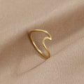 Imari Gold Wave Ring, lying on draped beige fabric, polished gold wave-shaped band