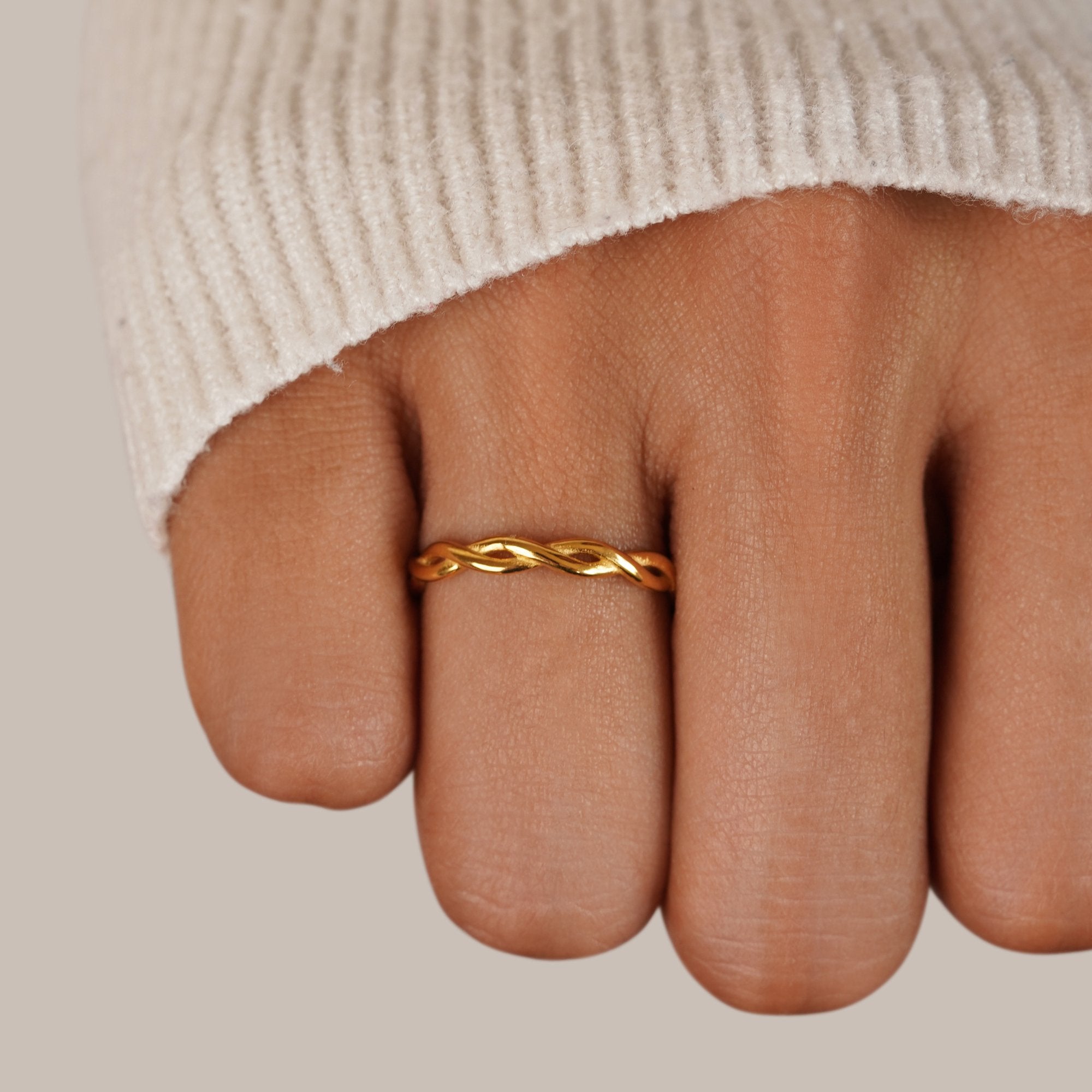 Infinity 18K Gold Twist Ring, worn on a finger of a hand in a cream knit sleeve