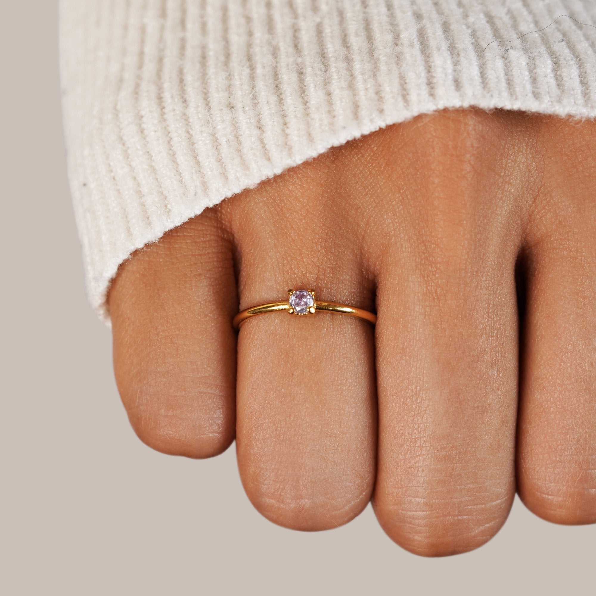 June Birthstone 18K Gold Ring, worn on a middle finger with a cream knit sleeve, small lilac stone