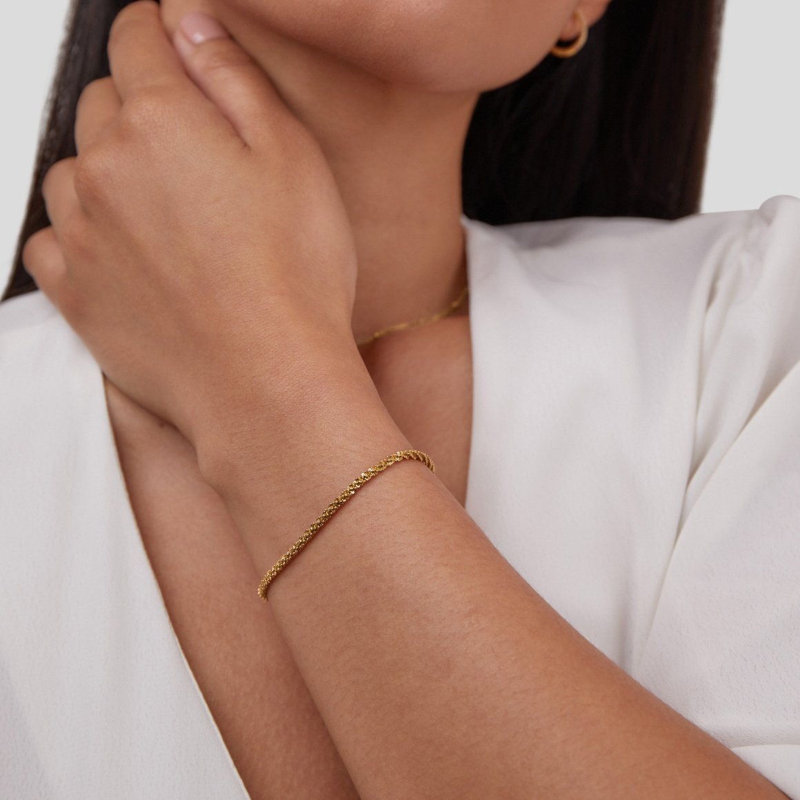 Kai 18K Gold Bracelet, worn on a wrist with a hoop earring and white top