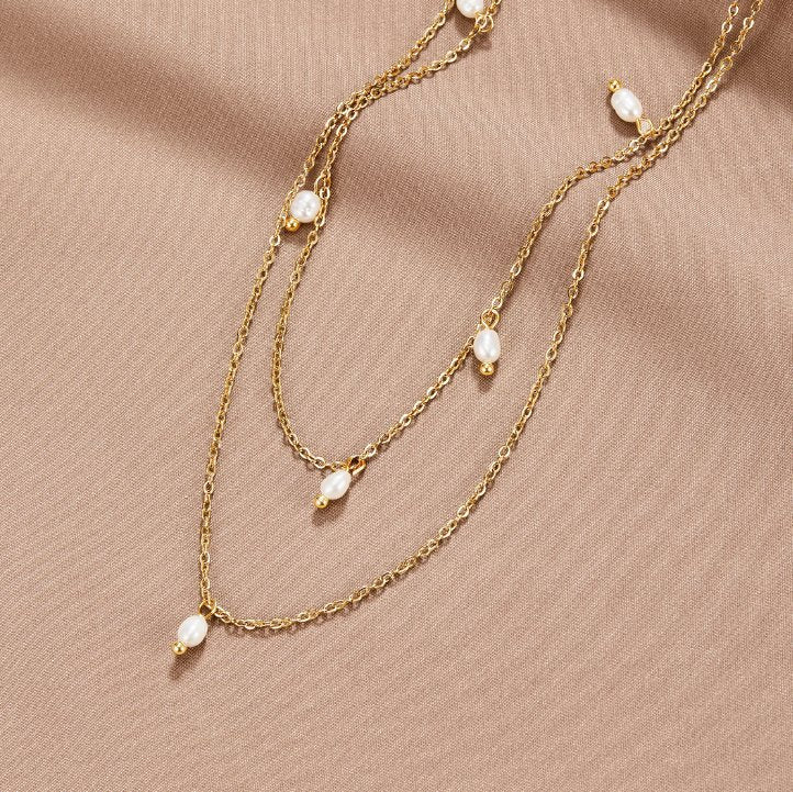 Kayla Pearl Drop Layered Necklace, two gold chains with small pearl drops, laid on beige fabric