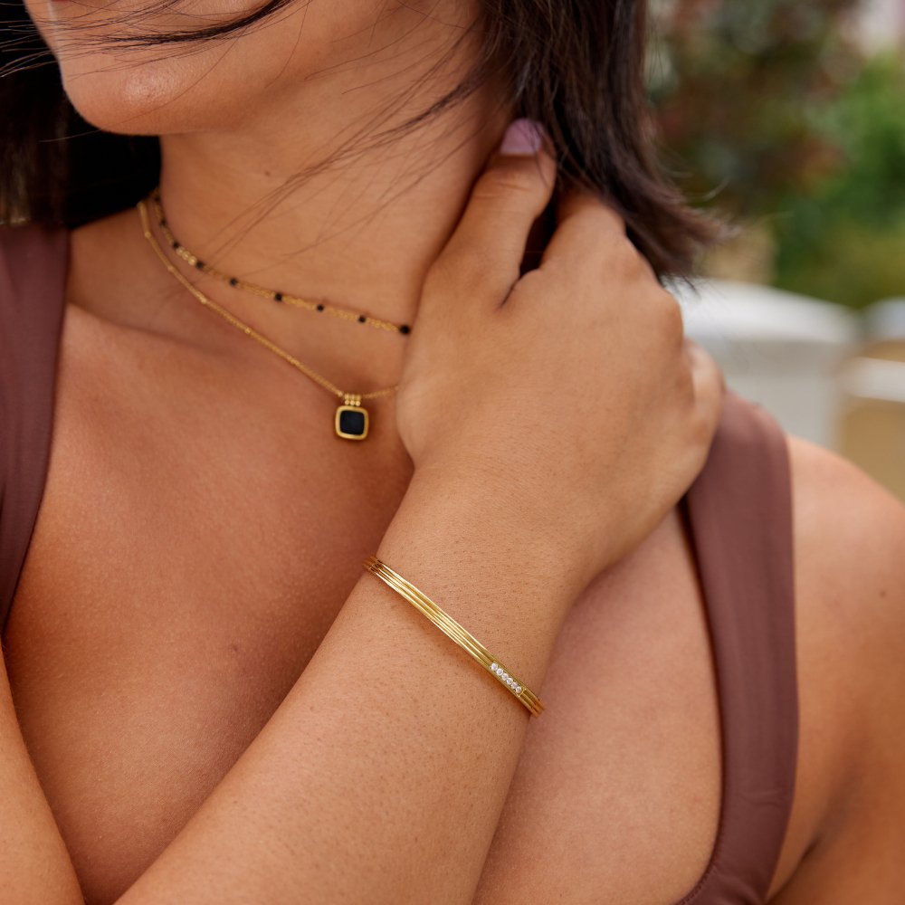 Kim Crystal bangle, worn on a wrist with a gold necklace and pendant