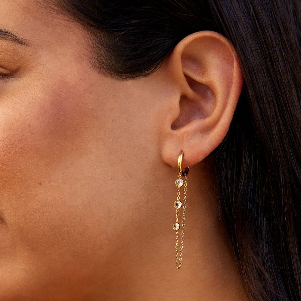 Kira Crystal Drop Hoop Earrings, worn on an ear with gold chains and small clear stones