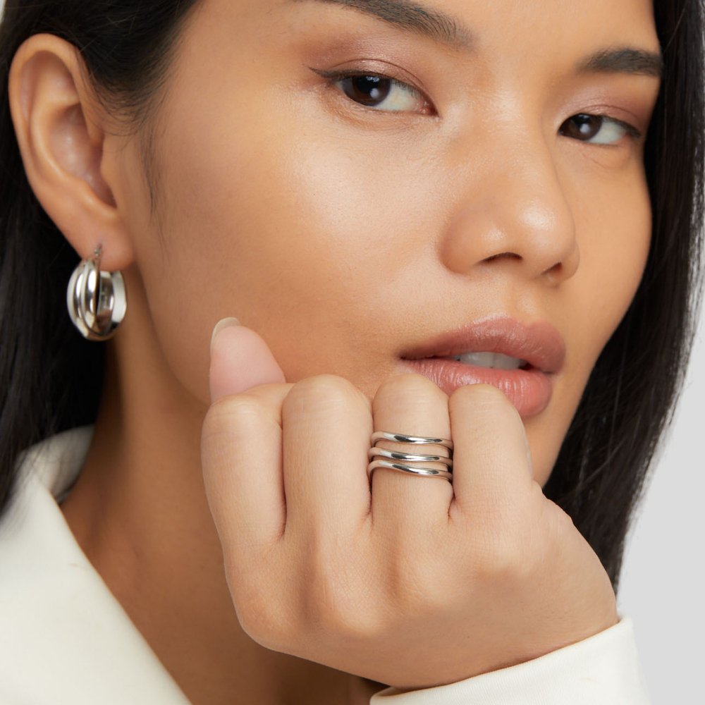 Kiya Layered Silver Ring, worn on a hand near the face, with matching silver hoop earring