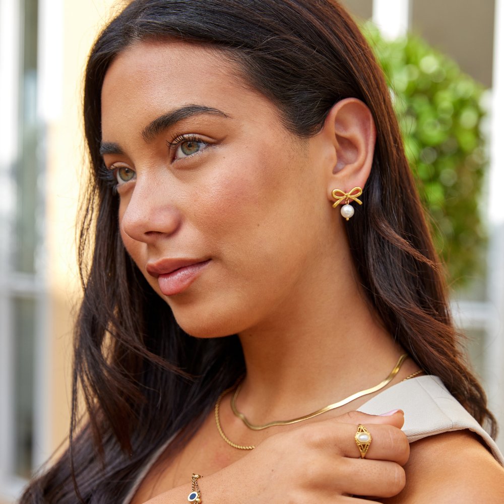 Laila Bow Pearl Earrings, worn on a model with a gold bow and pearl drop earring