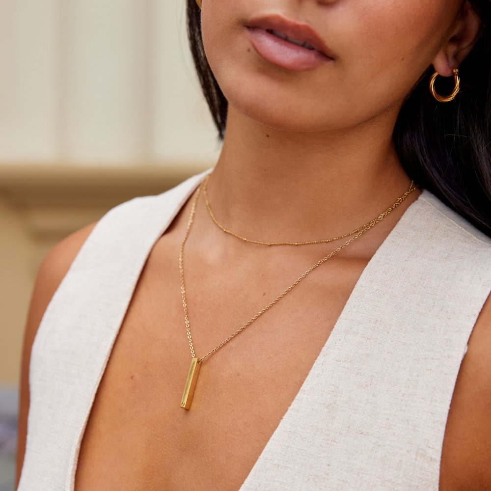 Lala Gold Bar Necklace, worn on a model with a gold hoop earring and layered chains
