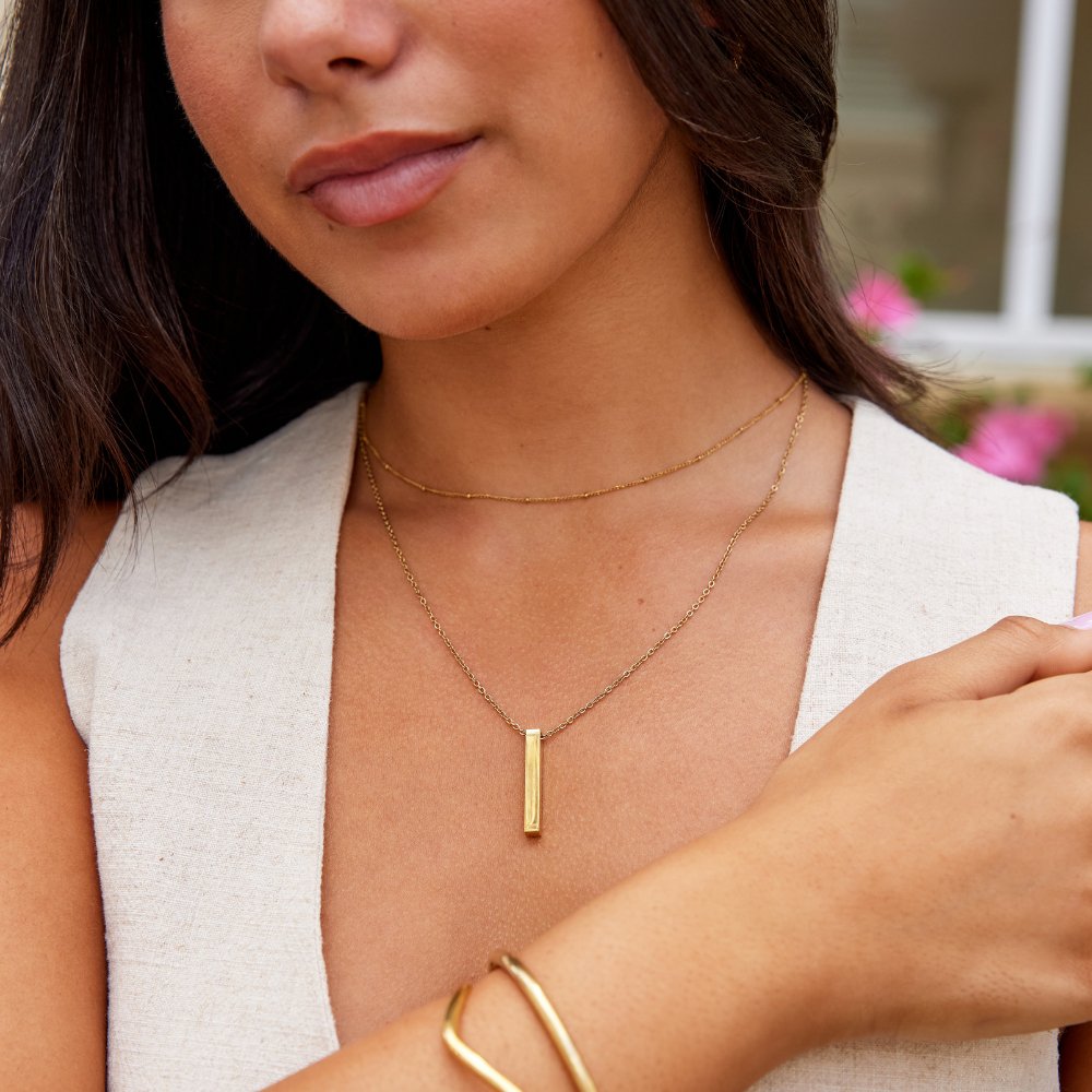 Lala Gold Bar Necklace, worn on a model with a layered gold chain and gold cuff bracelets